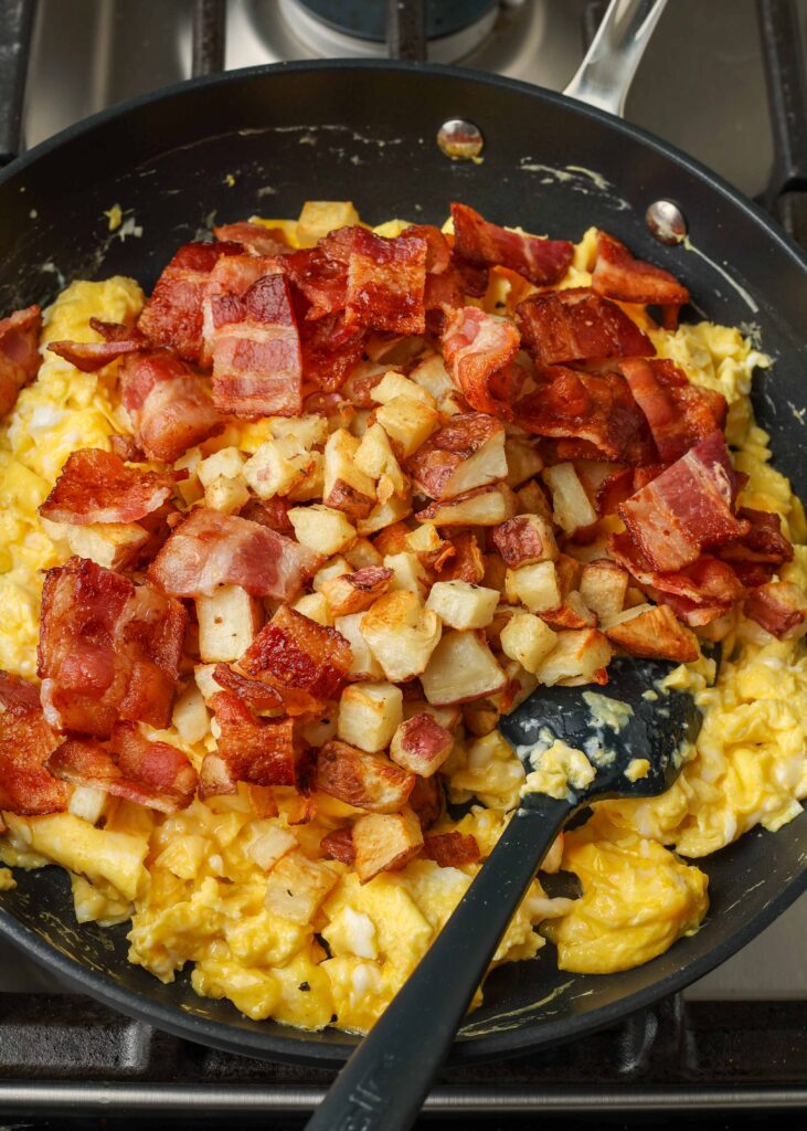 scrambled eggs with bacon and roasted potatoes in skillet