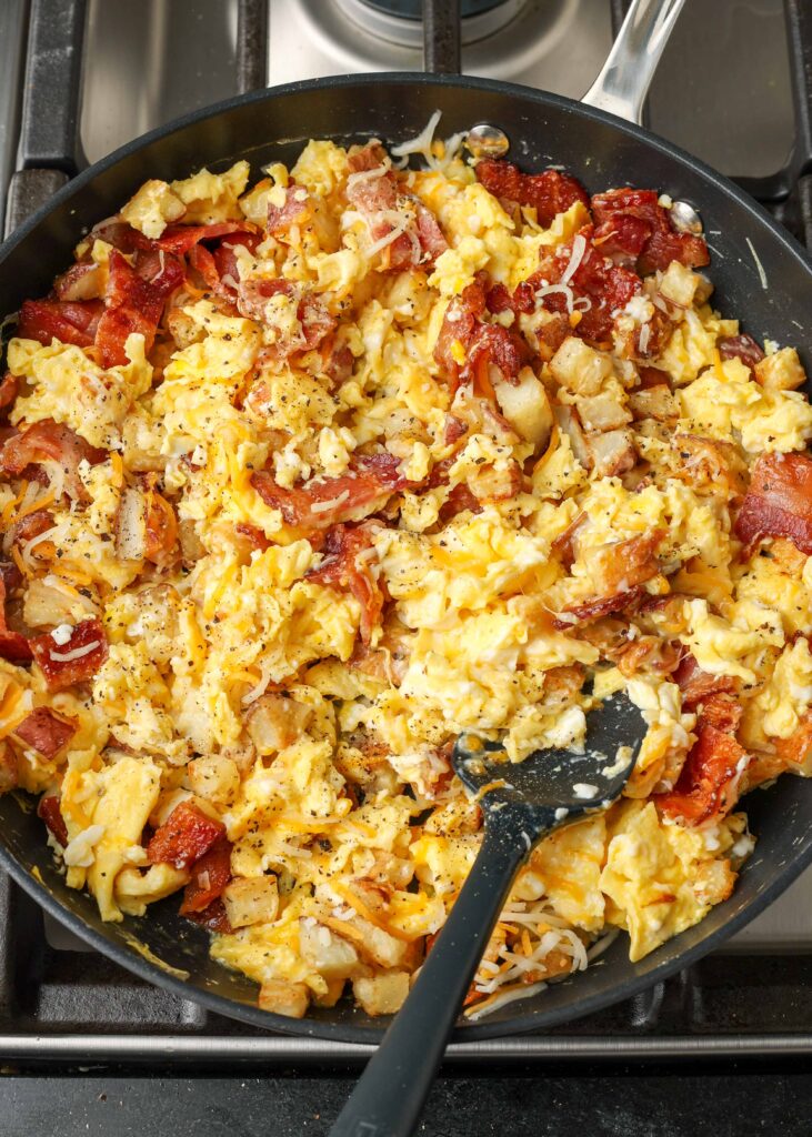 cheesy scrambled eggs with potatoes and bacon in skillet