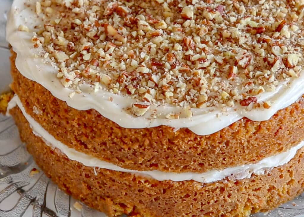 carrot cake topped with cream cheese frosting and sprinkled with pecans