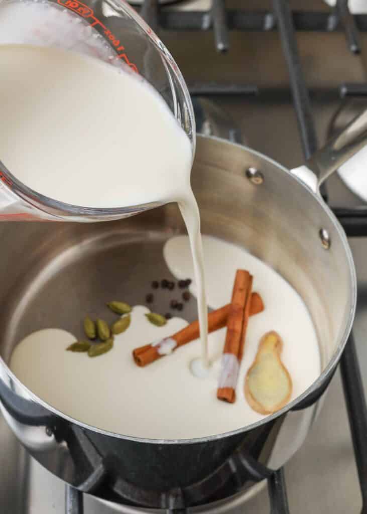 Pouring in the milk and heavy cream to heat with the spices