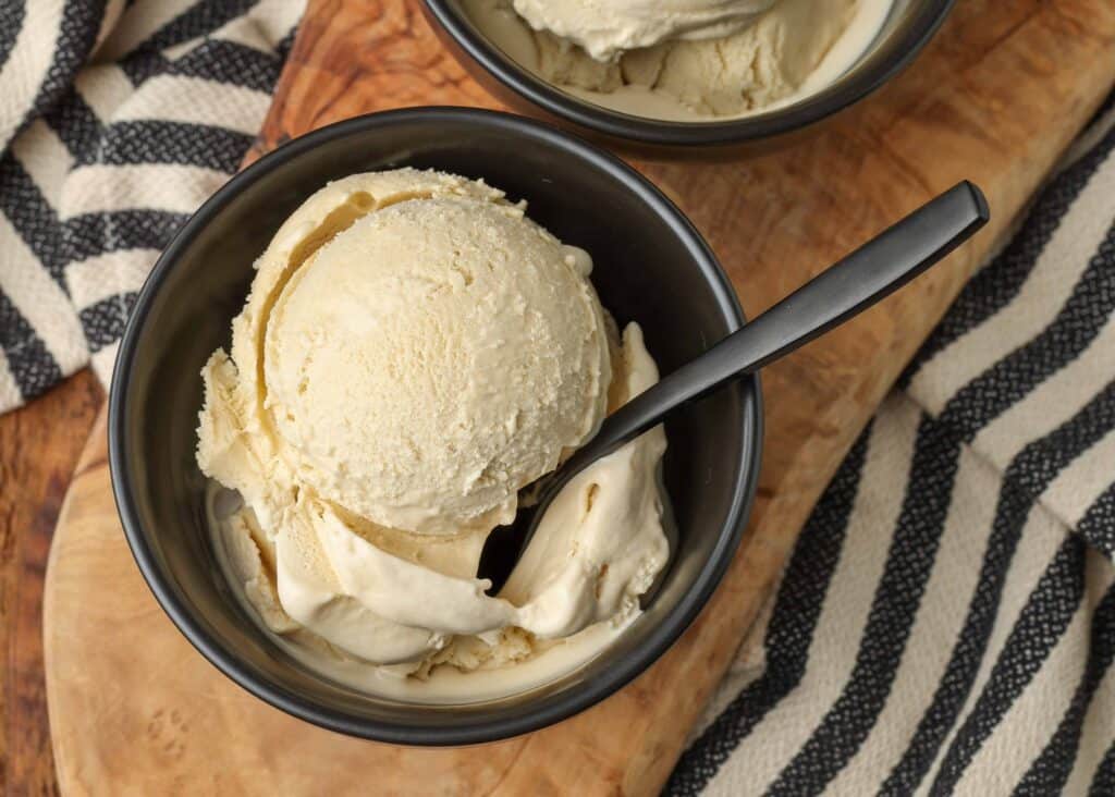 Overhead shot of coffee ice cream, served in a black bowl on a wooden cutting board with a black spoon