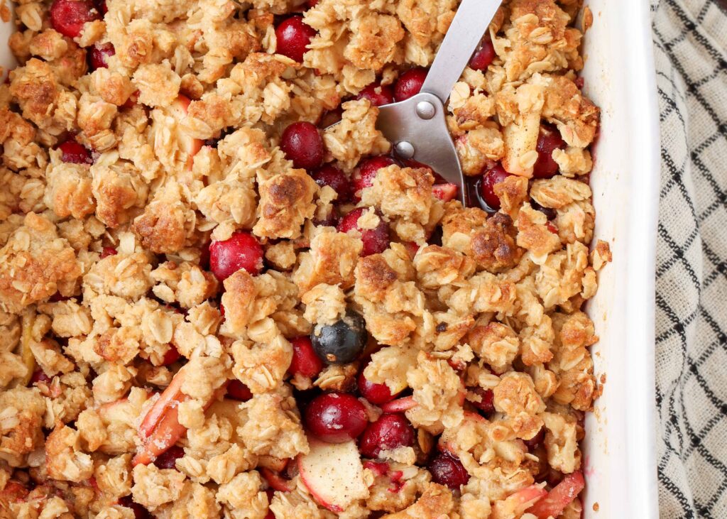apple crisp with cranberries in white baking dish with plaid towel