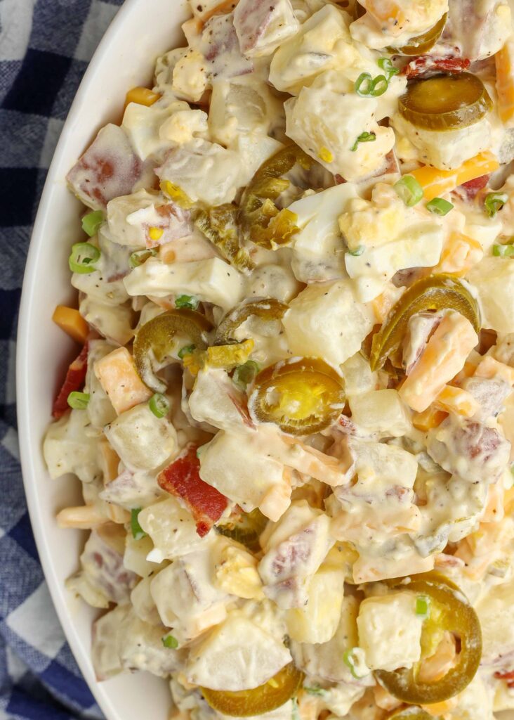 Near close-up of creamy jalapeno potato salad topped with bacon, cheese, green onions, and jalapenos, served in a white bowl
