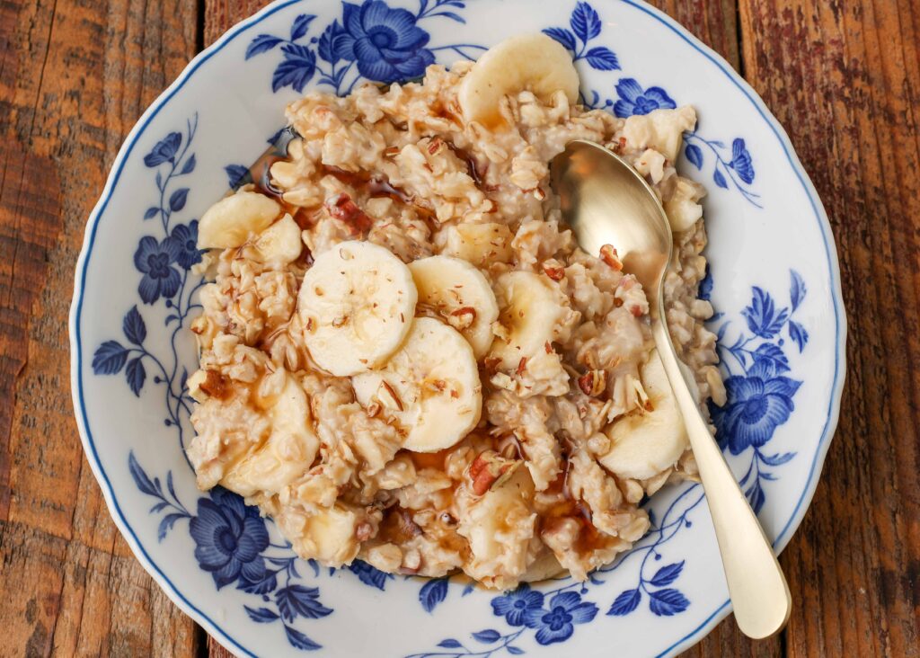Overhead close-up wide shot of maple banana nut oatmeal, served with a silver spoon in a white bowl with blue floral print