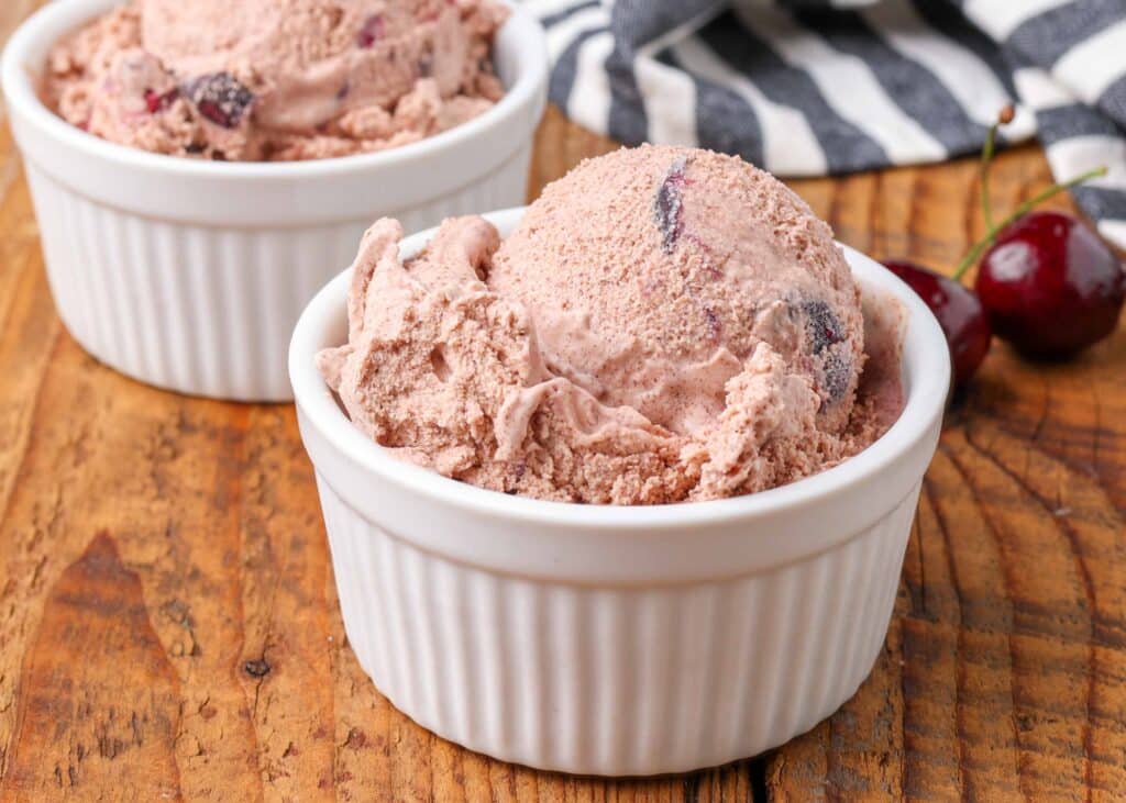 chocolate cherry ice cream in white bowl with cherries next to it