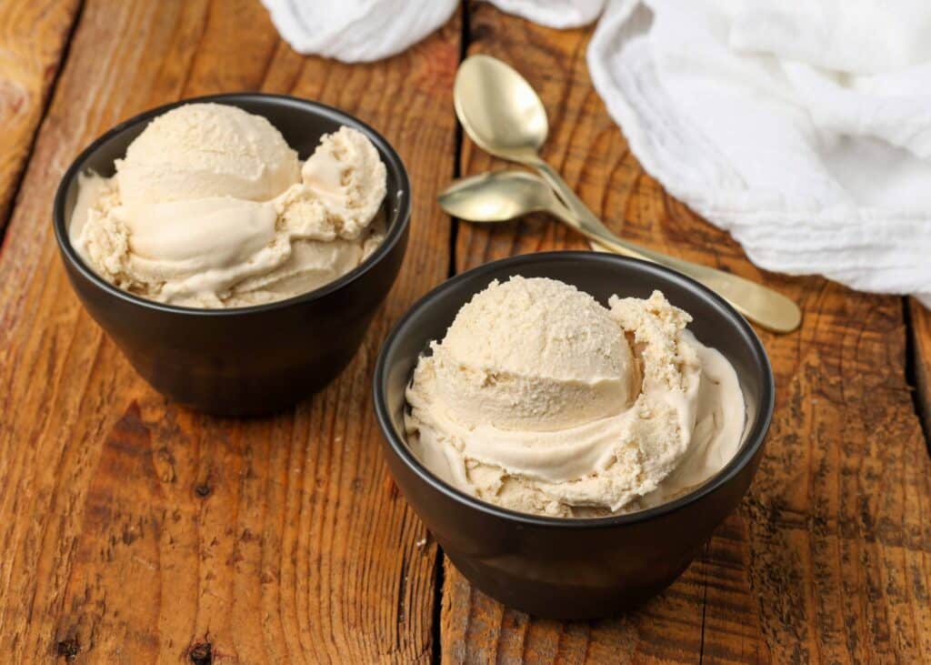 caramel ice cream in black bowls with gold spoons on wooden table