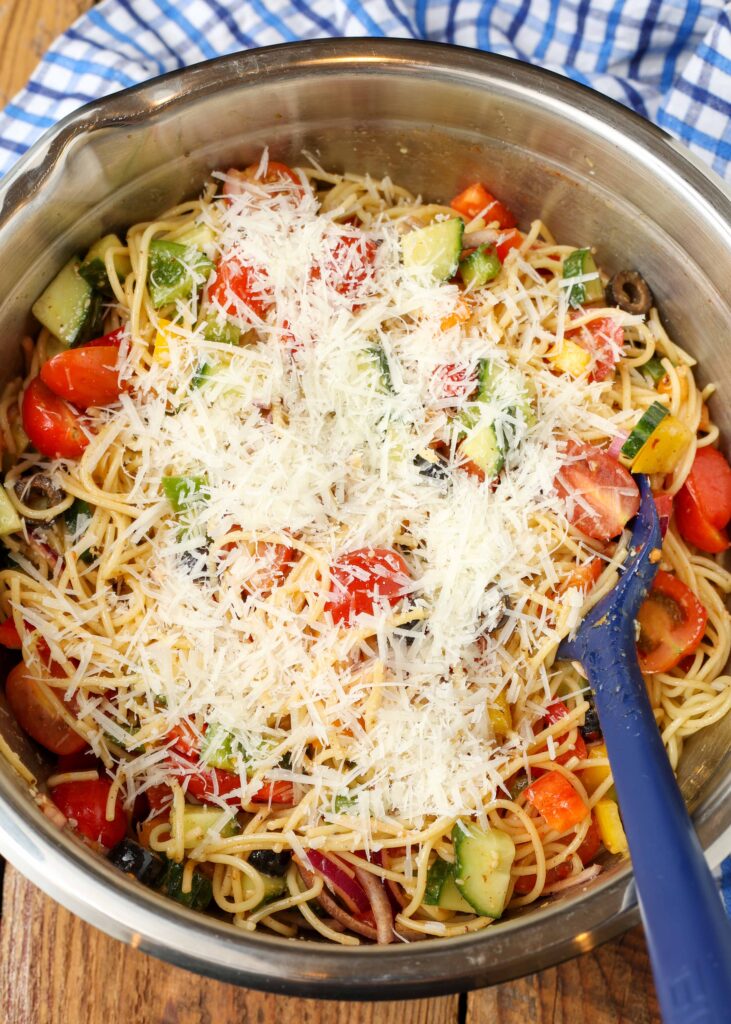 Fresh parmesan has been shredded over the other ingredients in this salad in a metal bowl, with a blue silicone spatula