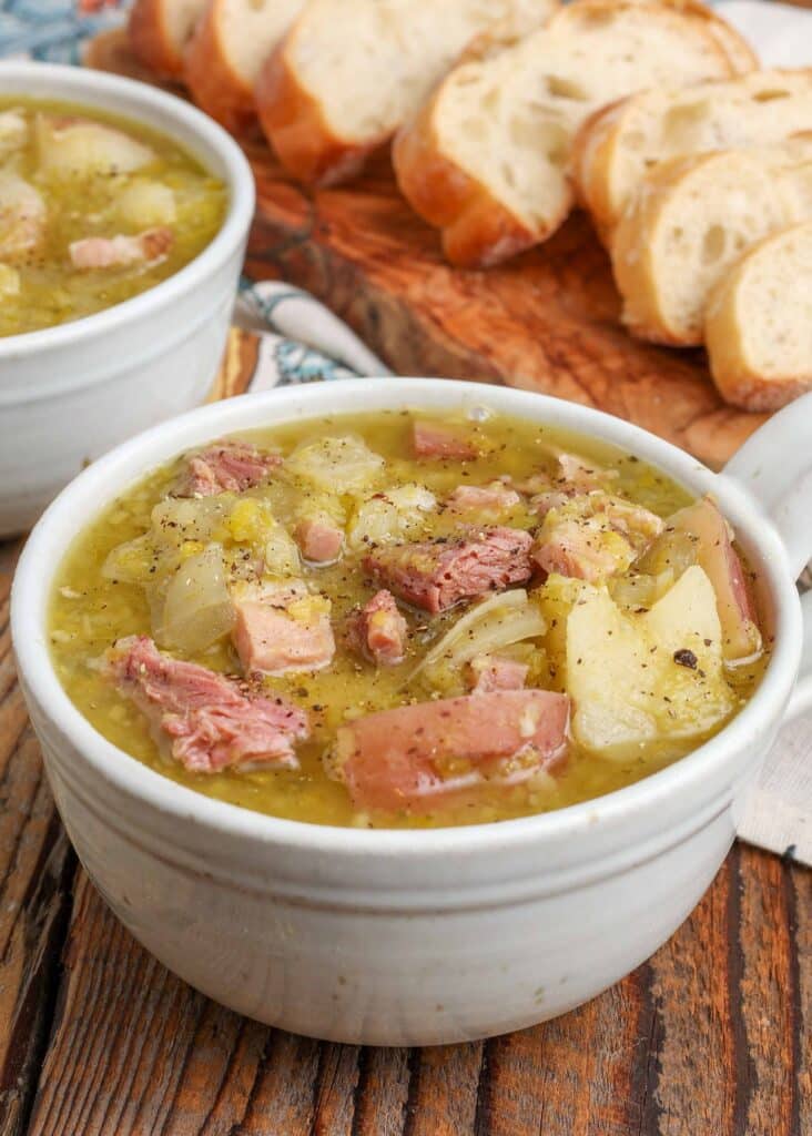 pea soup with ham and potatoes in mugs with sliced bread next to them