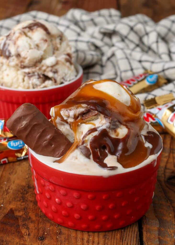 A fun size twix candy bar stick up from beside a scoop of ice cream that is drizzled with caramel and hot fudge in a red ramekin